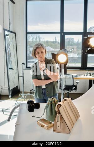 Middle-aged woman standing confidently and looking at bag in modern photo studio. Stock Photo