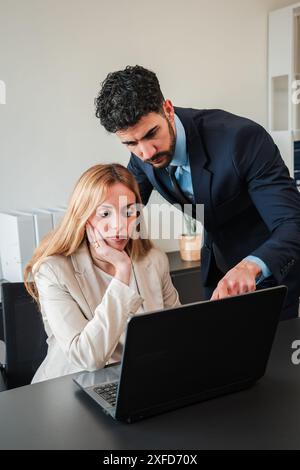 Vertical. Two real office colleagues working with a laptop on a work project. Partners colaborating at workplace. Businesspeople on a executive meeting. Coworkers using a computer. Teamwork planning. High quality photo Stock Photo