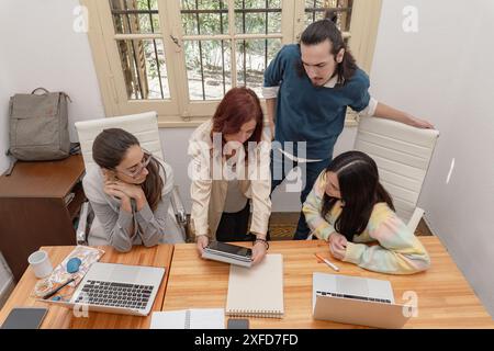 A diverse group of professionals collaborating in a modern office environment, reviewing documents and working on laptops. Stock Photo
