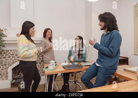A group of business professionals enjoying a coffee break while having a friendly conversation in a modern office environment, showing a relaxed and c Stock Photo