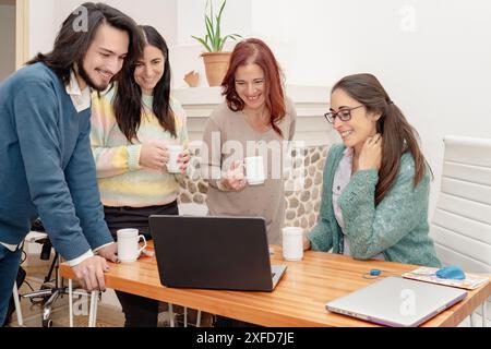 Smiling business professionals collaborate at a desk with a laptop in a creative office. They collaborate as a team, share ideas and work on projects Stock Photo