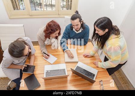 A group of four colleagues participates in a collaborative meeting, using laptops, notebooks and a tablet for discussion. Stock Photo