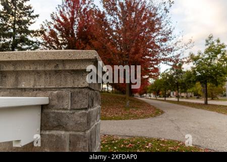 Grey brick wall - vibrant autumn backdrop with red and orange trees - pathway with fallen leaves - clear blue sky overhead. Taken in Toronto, Canada. Stock Photo