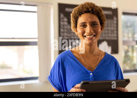 Holding tablet, smiling teacher standing in classroom at high school, copy space Stock Photo