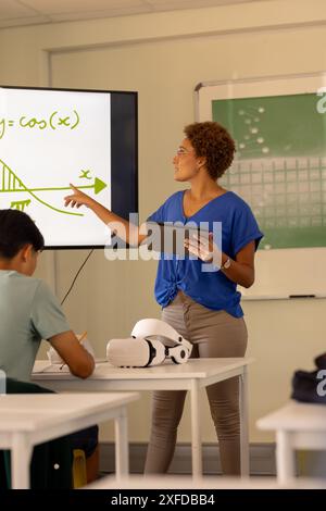 Teaching math, teacher using tablet and pointing at screen in high school classroom Stock Photo