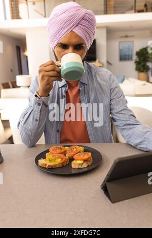 Drinking coffee and using tablet, man having breakfast with avocado toast Stock Photo