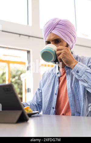Drinking coffee, man using tablet while eating breakfast at home Stock Photo