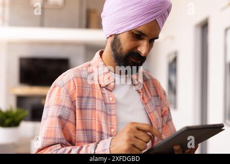 Using tablet, man in turban focusing on work at home Stock Photo