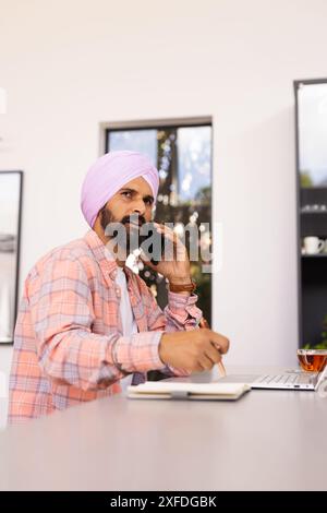 Talking on smartphone, man writing in notepad and using laptop at home Stock Photo
