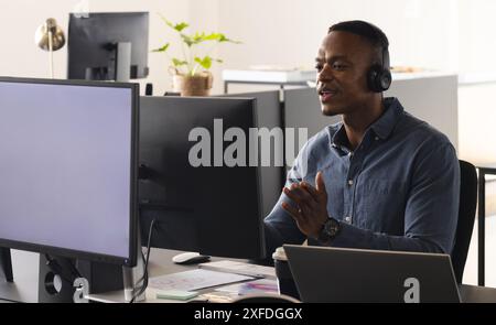 Using headset, man in office working on computer and having video call, copy space Stock Photo