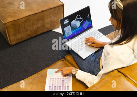 Using laptop, woman analyzing virtual reality data and pointing at chart in office Stock Photo