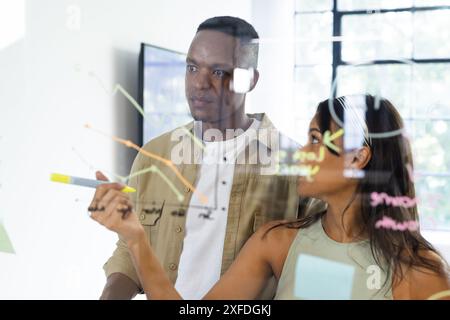 Collaborating on project, colleagues analyzing data on transparent board in office Stock Photo