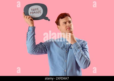 Thoughtful young man holding speech bubble with text DON'T FORGET on pink background Stock Photo