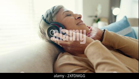 Retirement, senior woman and couch with headphones, relax and calm in living room, streaming music and audio. Rest, happy and mature lady with headset Stock Photo