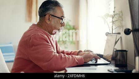 Senior man, laptop and typing at home for budget, planning and savings account for personal debt. Elderly person, computer and bills in living room Stock Photo