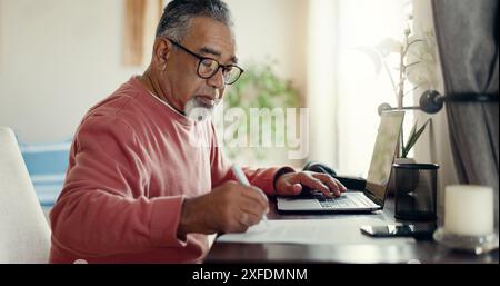 Senior man, laptop and writing at home for budget, planning and savings account for personal debt. Elderly person, computer and notebook in living Stock Photo