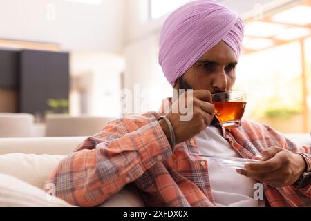 Drinking tea, man in turban relaxing on couch at home Stock Photo