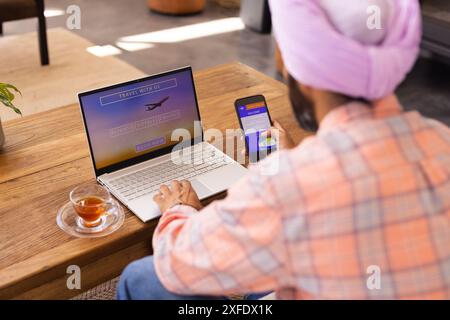 Booking travel online, man using laptop and smartphone at home with tea Stock Photo