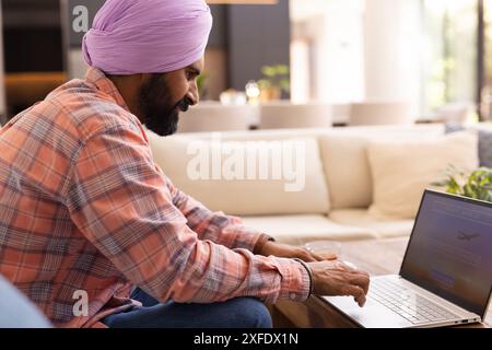 Typing on laptop, man in turban working from home on couch Stock Photo