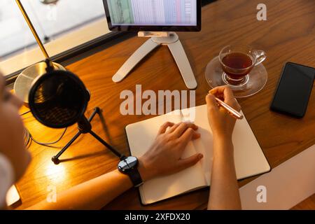 Recording podcast young woman writes in notebook at desk with tablet and microphone Stock Photo