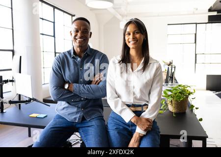 Sitting on desk in modern office, smiling colleagues looking confident and professional Stock Photo