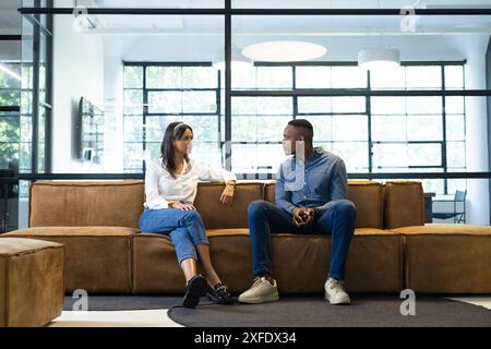 Having discussion, colleagues sitting on couch in modern office space Stock Photo