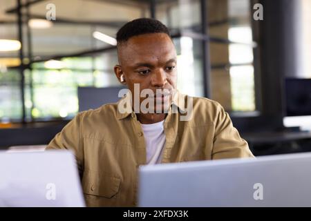Working in office, man using laptop and wearing wireless earbuds, concentrating Stock Photo