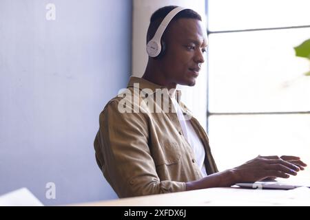 Wearing headphones, man working on laptop at modern office desk Stock Photo