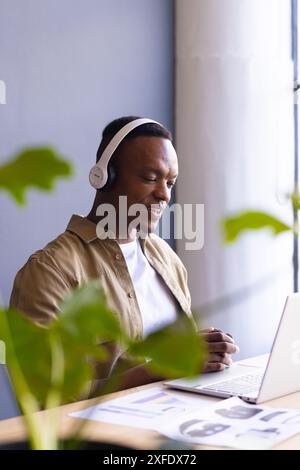 Using laptop and wearing headphones, man participating in virtual business meeting Stock Photo