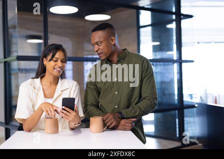 Colleagues in office, discussing work while looking at smartphone with coffee mugs Stock Photo