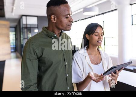 Discussing project, colleagues using digital tablet in modern office space Stock Photo
