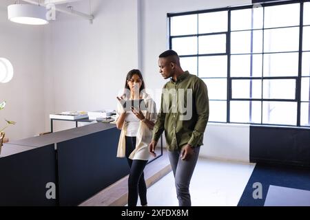 Discussing work, colleagues walking in modern office while using digital tablet Stock Photo