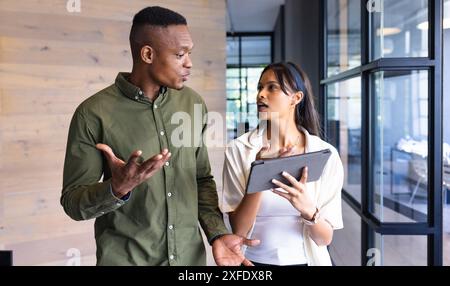 Discussing work, colleagues walking in office hallway with tablet in hand Stock Photo