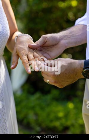 Exchanging wedding rings, senior bride and groom celebrating marriage ceremony outdoors with joy Stock Photo