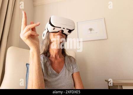 Using VR headset, mature woman interacting with virtual environment at home Stock Photo