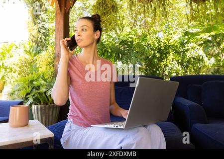 Working from home, woman using laptop and talking on smartphone outdoors Stock Photo