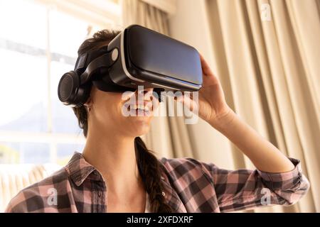 Using VR headset, young woman experiencing virtual reality at home Stock Photo