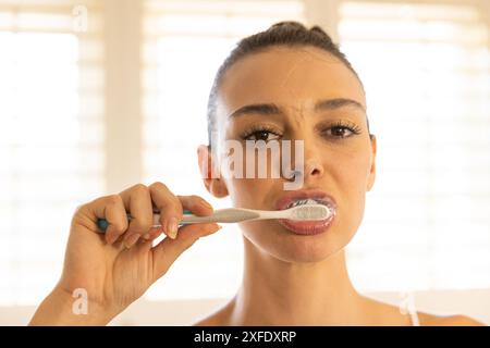 Brushing teeth, young woman focusing on dental hygiene in bathroom Stock Photo