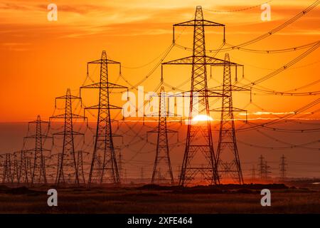 Sun setting behind the electric power lines running from Dungeness power station on the Kent coast south east England UK Stock Photo