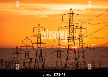 Sun setting behind the electric power lines running from Dungeness power station on the Kent coast south east England UK Stock Photo