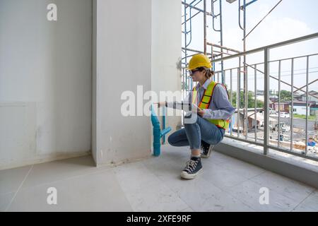 A construction worker is inspecting a building site. They are wearing safety gear and checking plumbing installation indoor. Stock Photo