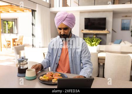 Working from home, man using tablet while having breakfast with coffee Stock Photo