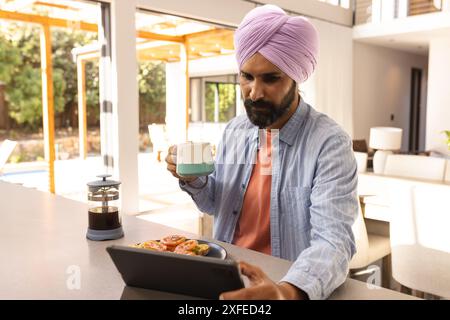 Drinking coffee and using tablet, man enjoying breakfast at home Stock Photo