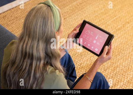 Using tablet, mature woman controlling smart home devices in living room Stock Photo