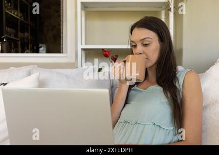 Drinking coffee while using laptop, young woman working from home Stock Photo