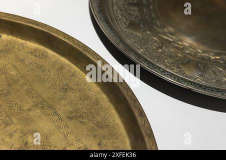 Ancient copper trays with embossed arabic patterns stand on a white table, close up photo with selective soft focus Stock Photo