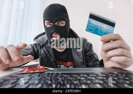 a male thief holds a credit card in his hand and picks up a password to steal money. theft from electronic wallets Stock Photo