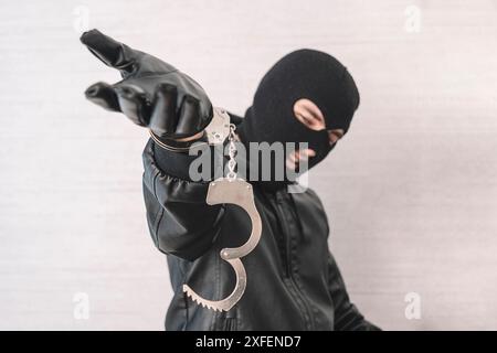 a bandit in a black mask and gloves with handcuffs in his hands on a white background. Release from imprisonment. Prison break concept. Jailbreak Stock Photo
