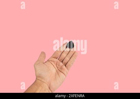 Black male hand holding a guitar pick isolated on pink background Stock Photo