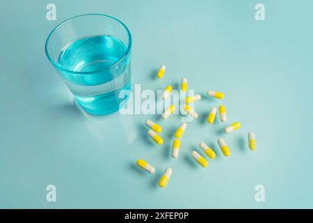 Glass of water and white pills on blue background with hard light . Creative. White tablets and drink on blue background. Medicine autumn vitamins and Stock Photo